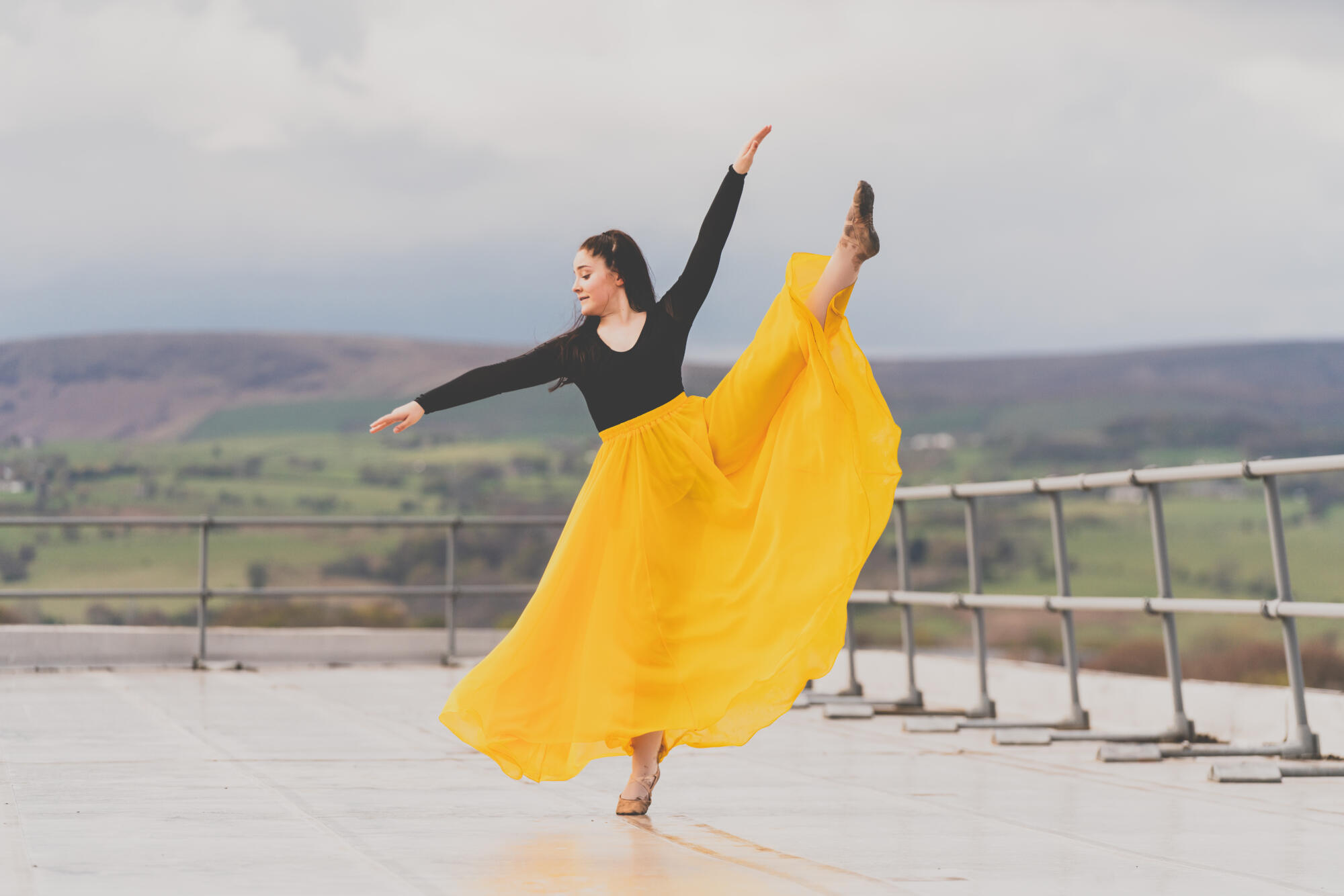 A spectacular shot of a dancer in a bright yellow skirt on to of a building with the skyline of Burnley n the background