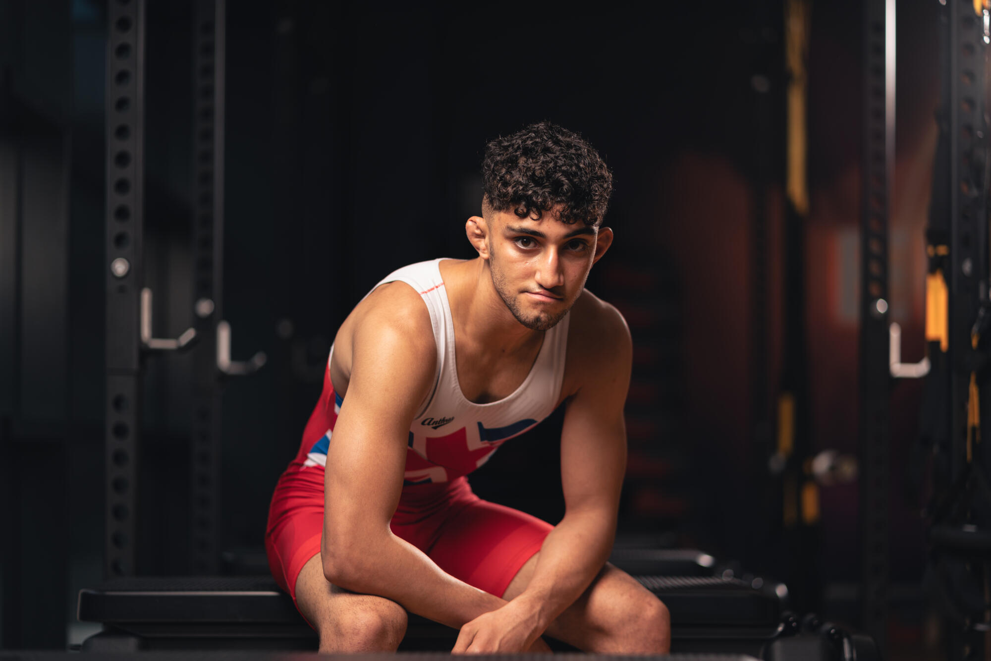 A wrestler sits in portrait in a dark training room.