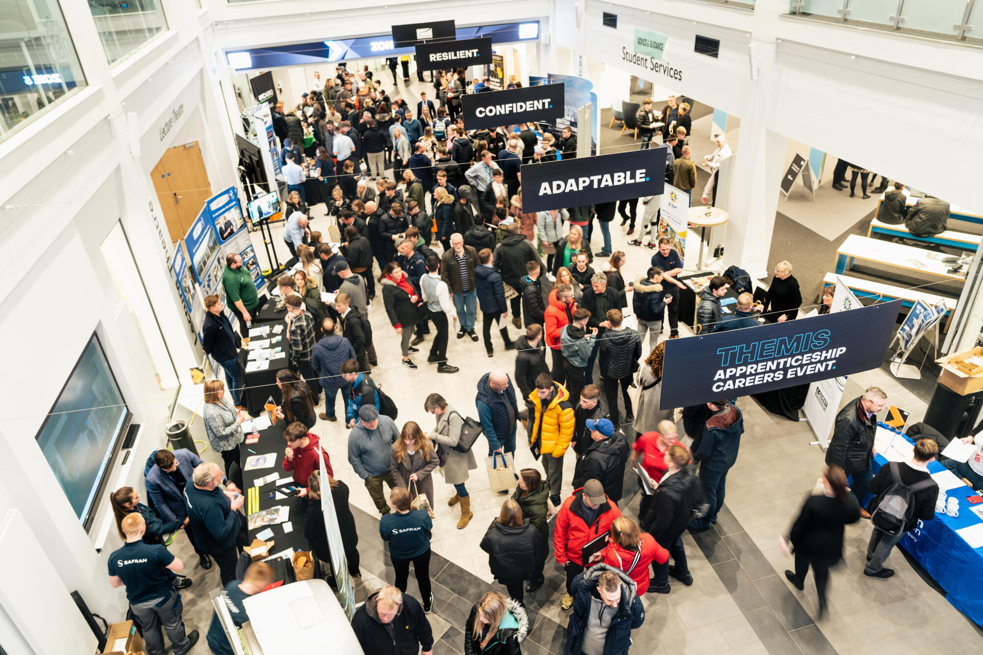 A crowded atrium at a modern UK college during a careers expo