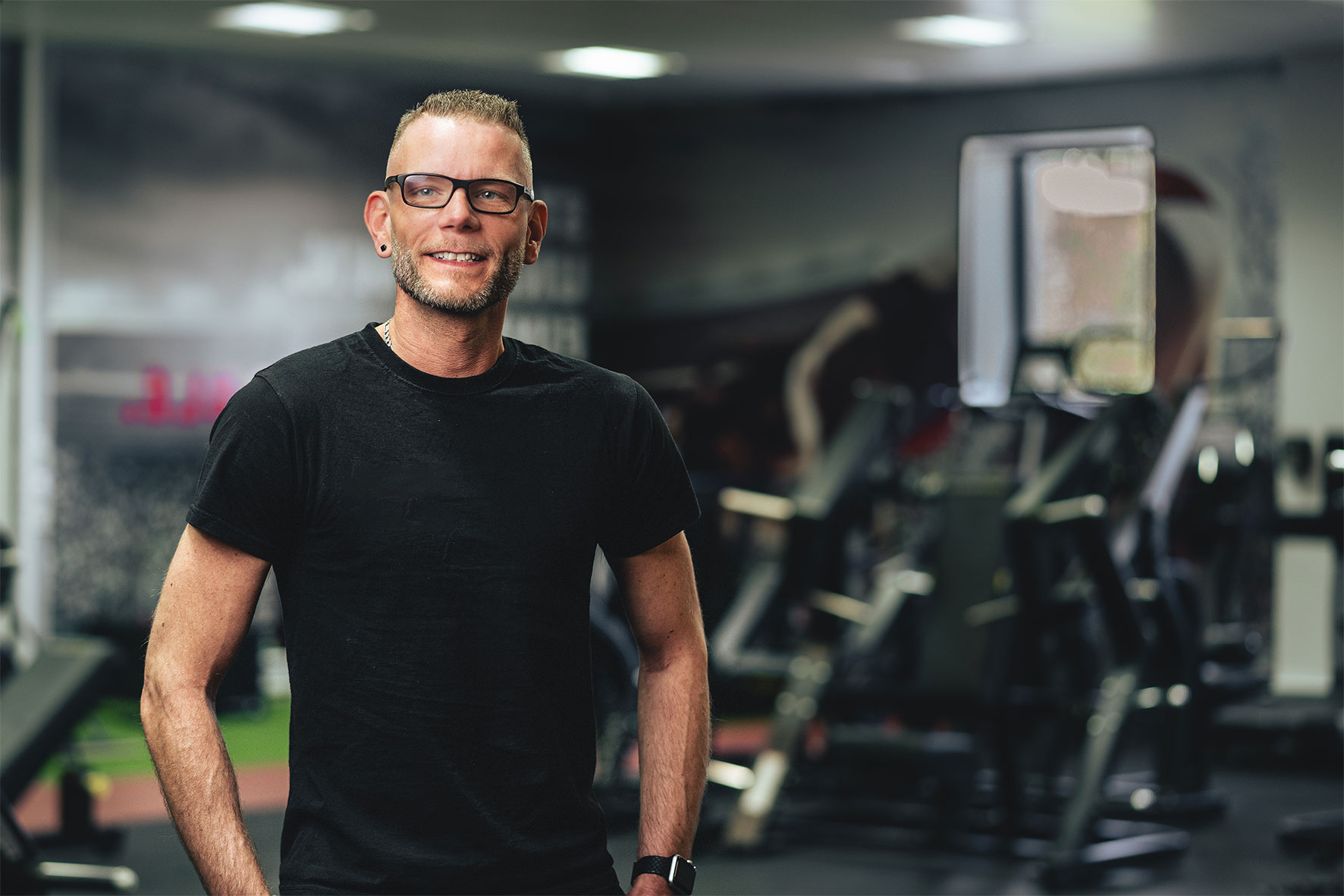 Man standing next in a gym surrounded by exercise machines smiling at the camera